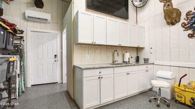 kitchen featuring a wall unit AC, light stone countertops, white cabinetry, and a sink