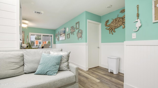 living area with a wainscoted wall, wood finished floors, and visible vents