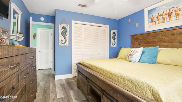 bedroom featuring ceiling fan, wood finished floors, visible vents, baseboards, and a closet