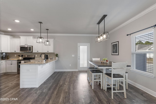 kitchen with appliances with stainless steel finishes, white cabinets, hanging light fixtures, and a kitchen breakfast bar