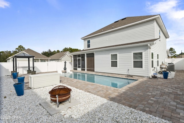 rear view of house with a sunroom, a fenced backyard, a fire pit, and a gazebo