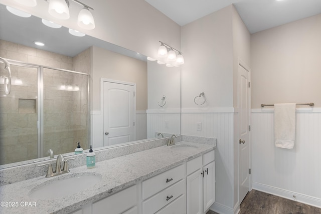 full bathroom featuring double vanity, a wainscoted wall, a shower stall, and a sink