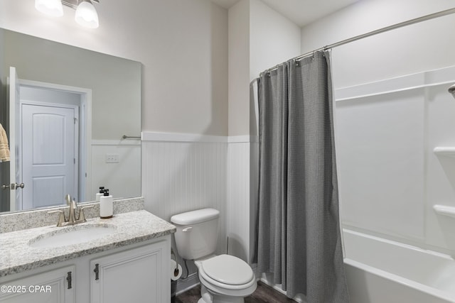 bathroom with a wainscoted wall, vanity, toilet, and shower / bath combo with shower curtain