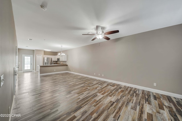 unfurnished living room with wood-type flooring and ceiling fan with notable chandelier