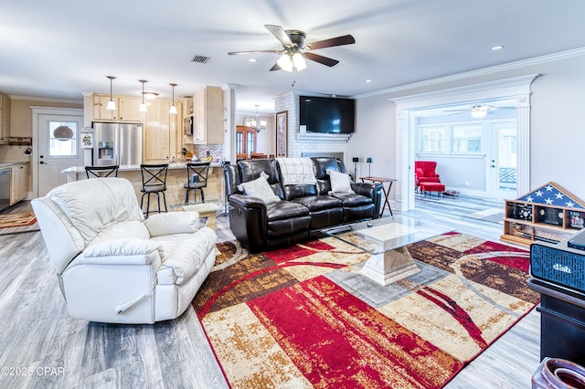 living room with crown molding, a fireplace, ceiling fan with notable chandelier, and light hardwood / wood-style floors