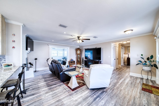 living room with hardwood / wood-style flooring, a fireplace, crown molding, and ceiling fan