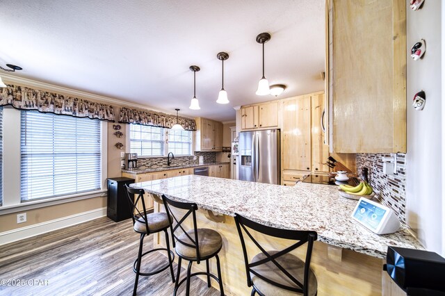 kitchen with a breakfast bar, light brown cabinetry, hanging light fixtures, appliances with stainless steel finishes, and kitchen peninsula