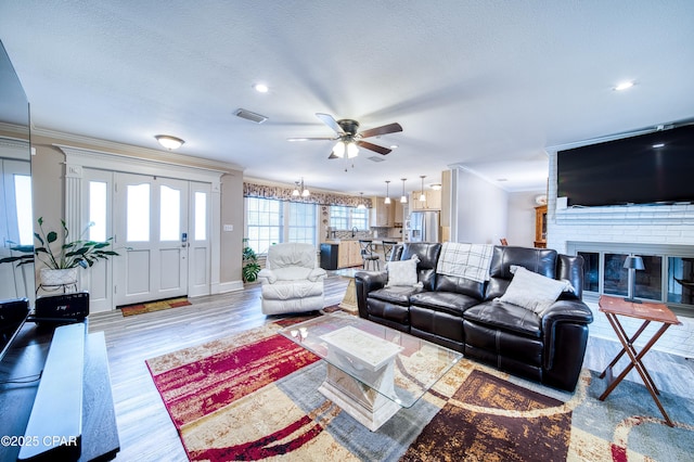 living room with a fireplace, ornamental molding, ceiling fan, light hardwood / wood-style floors, and a textured ceiling