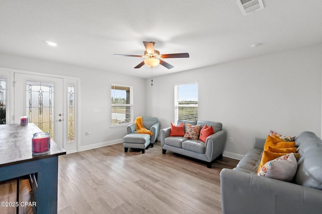 living area featuring a ceiling fan, visible vents, baseboards, and wood finished floors