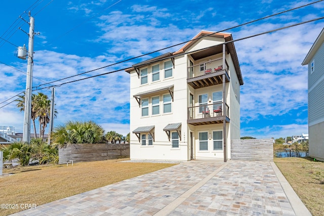 view of front of home featuring fence, a balcony, a front lawn, and stucco siding