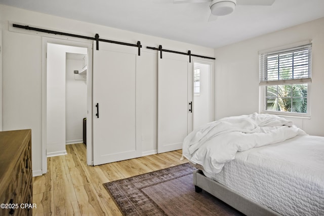 bedroom featuring a walk in closet, ceiling fan, a barn door, and light hardwood / wood-style floors