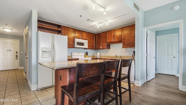 kitchen featuring sink, light tile patterned floors, white appliances, a center island, and light stone countertops