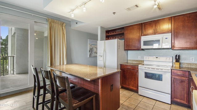 kitchen with white appliances, a breakfast bar area, stone counters, a kitchen island, and light tile patterned flooring