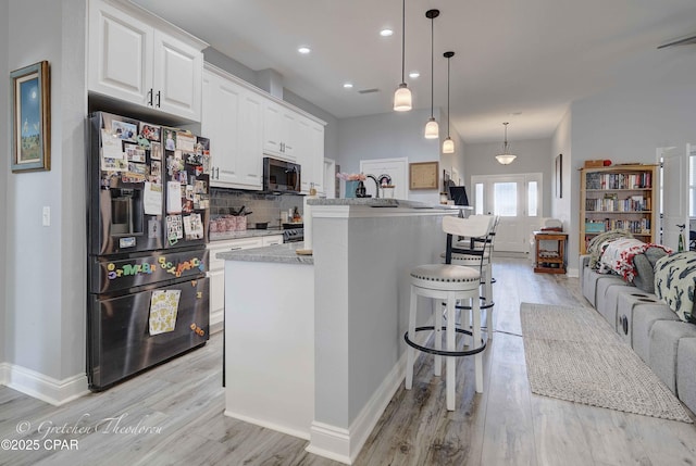 kitchen with a breakfast bar area, stainless steel appliances, decorative backsplash, white cabinets, and decorative light fixtures