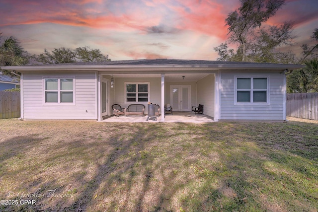 back house at dusk featuring a lawn and a patio