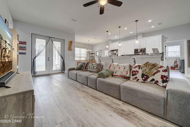 living room featuring ceiling fan with notable chandelier, light hardwood / wood-style floors, and french doors