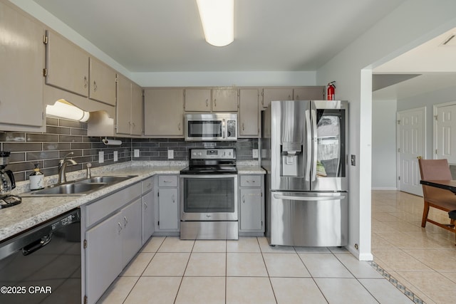 kitchen with a sink, backsplash, appliances with stainless steel finishes, light countertops, and light tile patterned floors