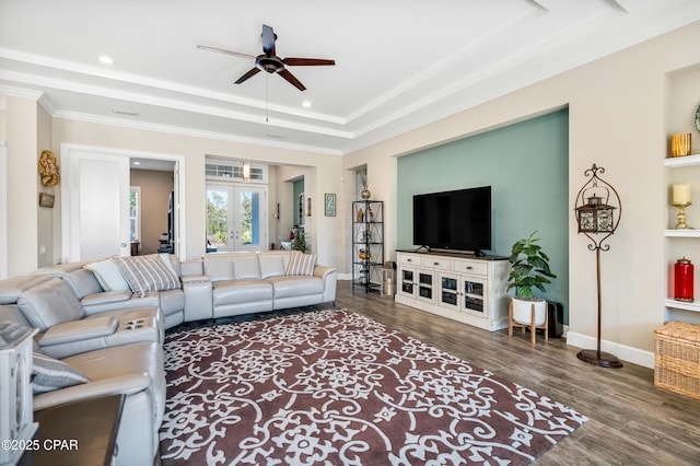 living area with a raised ceiling, crown molding, baseboards, and wood finished floors