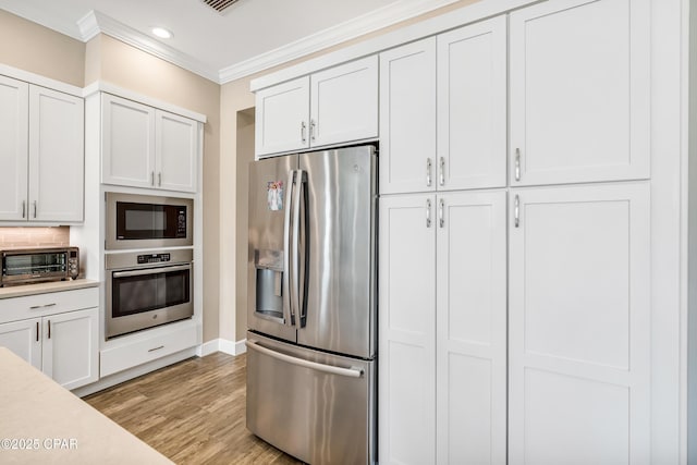 kitchen with a toaster, light countertops, light wood-style flooring, appliances with stainless steel finishes, and ornamental molding