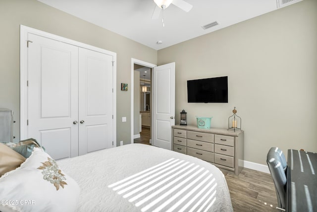 bedroom featuring ceiling fan, wood finished floors, visible vents, baseboards, and a closet