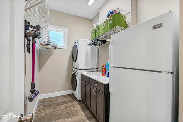 washroom featuring cabinet space, wood finished floors, stacked washer and clothes dryer, and baseboards