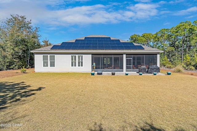 back of house with a sunroom, a lawn, roof mounted solar panels, and stucco siding