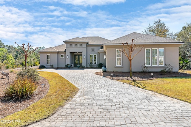 prairie-style home featuring a front yard, french doors, decorative driveway, and stucco siding