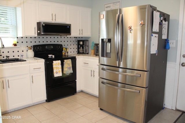 kitchen with tile countertops, appliances with stainless steel finishes, a sink, and white cabinets