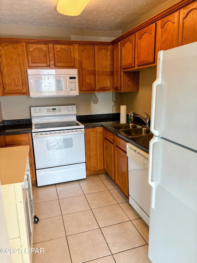 kitchen with dark countertops, white appliances, a sink, and light tile patterned floors