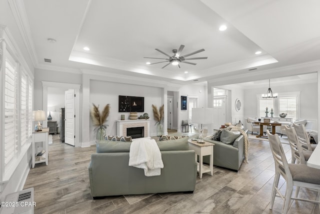 living room featuring ceiling fan with notable chandelier, a tray ceiling, light hardwood / wood-style floors, and crown molding