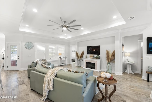 living room featuring light hardwood / wood-style flooring, ornamental molding, a raised ceiling, and ceiling fan