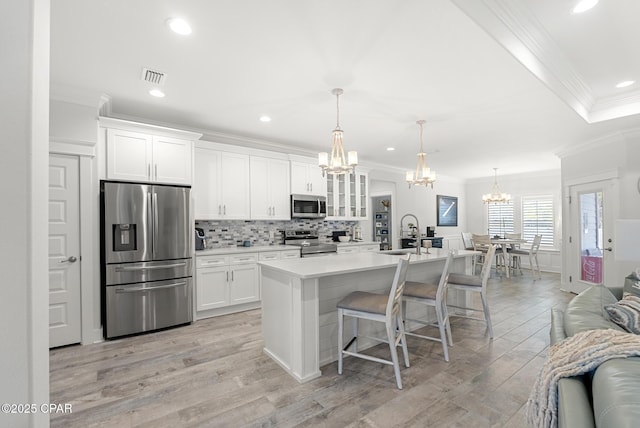 kitchen with a kitchen bar, white cabinetry, decorative light fixtures, appliances with stainless steel finishes, and an island with sink