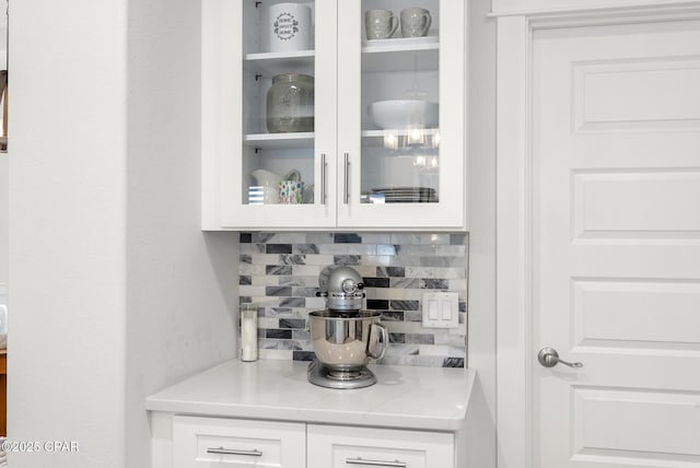 bar with white cabinetry, backsplash, and light stone counters