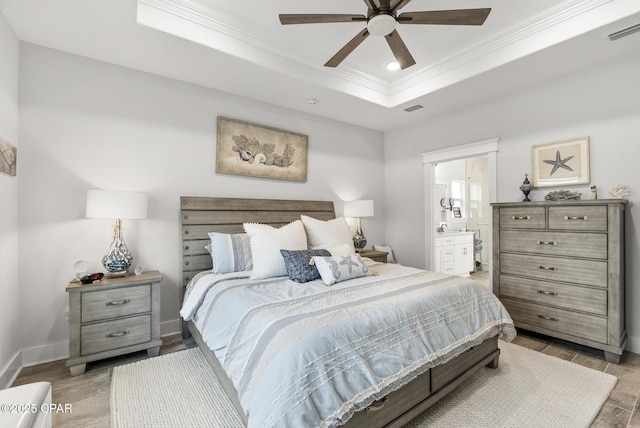 bedroom with light hardwood / wood-style flooring, ceiling fan, ensuite bathroom, a tray ceiling, and ornamental molding