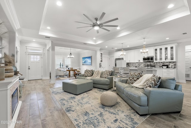 living room featuring ceiling fan with notable chandelier, sink, light hardwood / wood-style floors, a tray ceiling, and crown molding