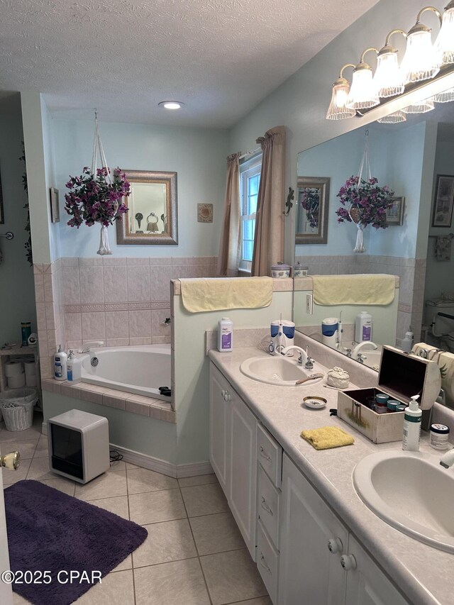 full bath featuring a sink, tile patterned flooring, tiled bath, and a textured ceiling