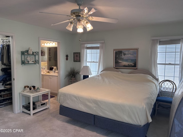 bedroom with a closet, connected bathroom, a walk in closet, ceiling fan, and light colored carpet