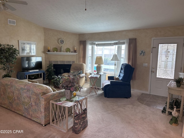 carpeted living area featuring a textured ceiling, visible vents, lofted ceiling, a tile fireplace, and ceiling fan