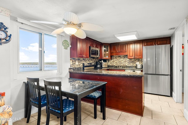 kitchen with stainless steel appliances, visible vents, backsplash, dark stone countertops, and a peninsula