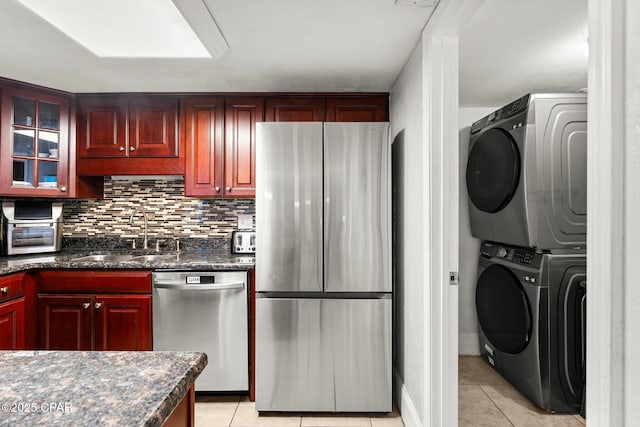 kitchen with stacked washer and dryer, light tile patterned floors, appliances with stainless steel finishes, and a sink