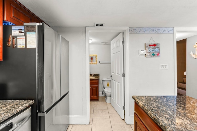 kitchen featuring dark stone counters, visible vents, light tile patterned flooring, and freestanding refrigerator