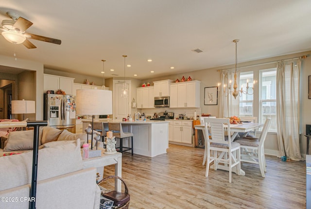 kitchen featuring stainless steel appliances, white cabinetry, a kitchen breakfast bar, light wood-style floors, and backsplash