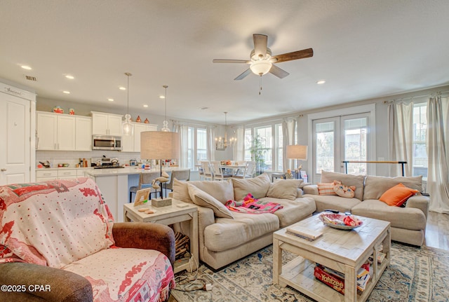 living room featuring ceiling fan with notable chandelier, a healthy amount of sunlight, visible vents, and light wood-type flooring