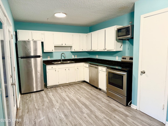 kitchen featuring sink, white cabinetry, stainless steel appliances, a textured ceiling, and light wood-type flooring