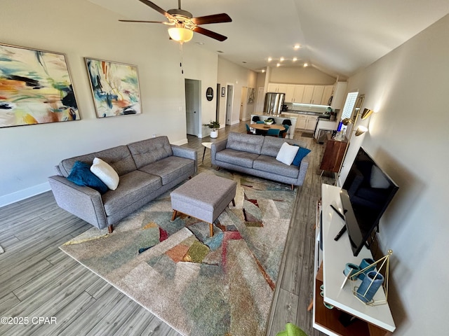 living area featuring a ceiling fan, vaulted ceiling, baseboards, and wood finished floors