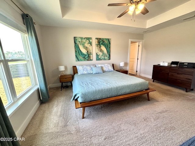 carpeted bedroom with ceiling fan, a raised ceiling, visible vents, and baseboards