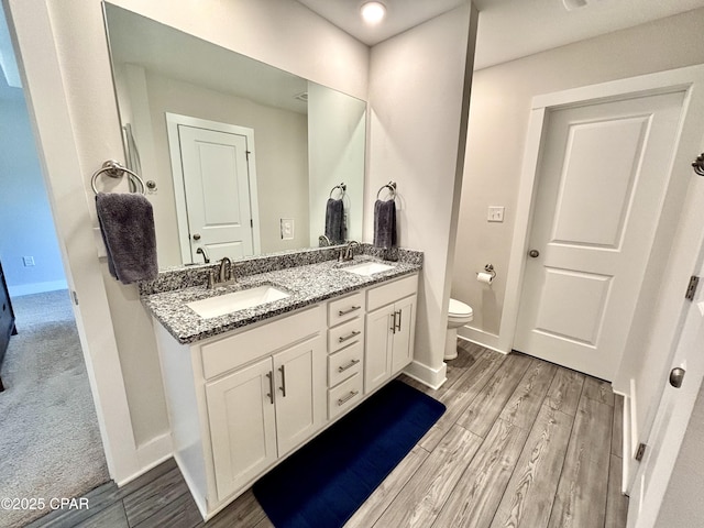 bathroom with wood finished floors, a sink, toilet, and double vanity