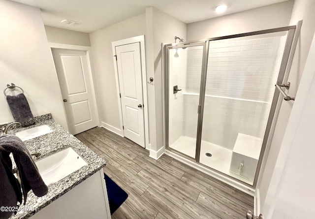 full bathroom with double vanity, wood finished floors, a stall shower, and a sink