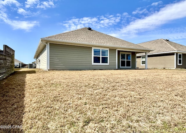 rear view of property with roof with shingles, cooling unit, and a lawn