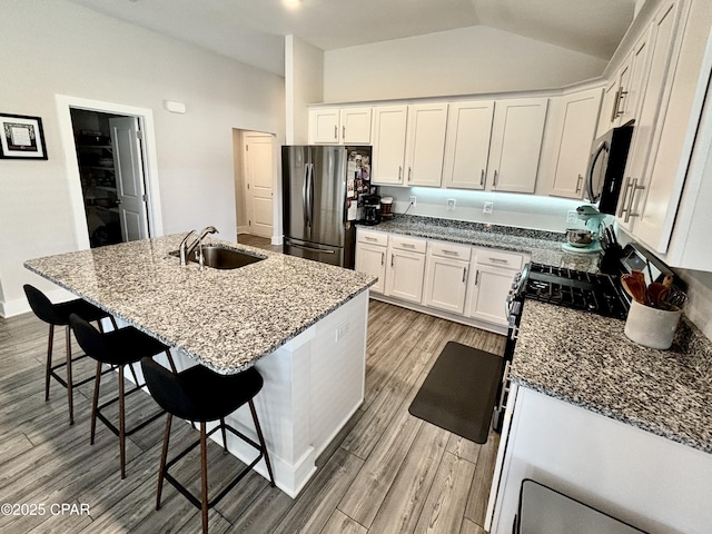 kitchen with dark stone counters, lofted ceiling, light wood-style flooring, stainless steel appliances, and a sink